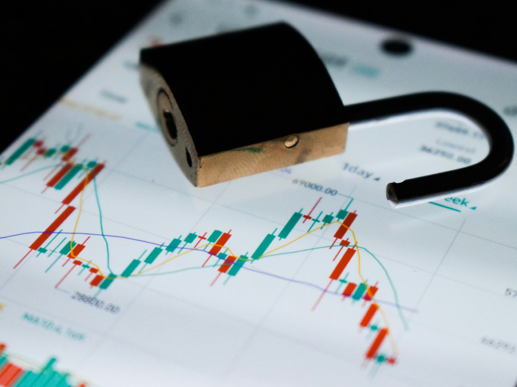 Cadeado aberto repousando sobre a tela de um smartphone que exibe gráficos de velas (candlestick) do mercado financeiro, simbolizando a segurança e a transparência nas transações digitais e investimentos.