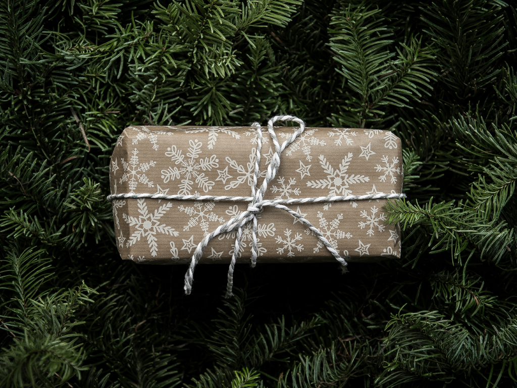 Presente de Natal embrulhado com papel decorado com flocos de neve e fita de cetim em meio a ramos de árvores de Natal.