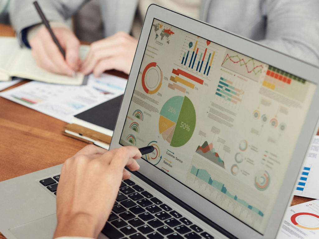 Homem analisando gráficos de dados em um laptop durante uma reunião de negócios, com foco em análises financeiras e estatísticas.