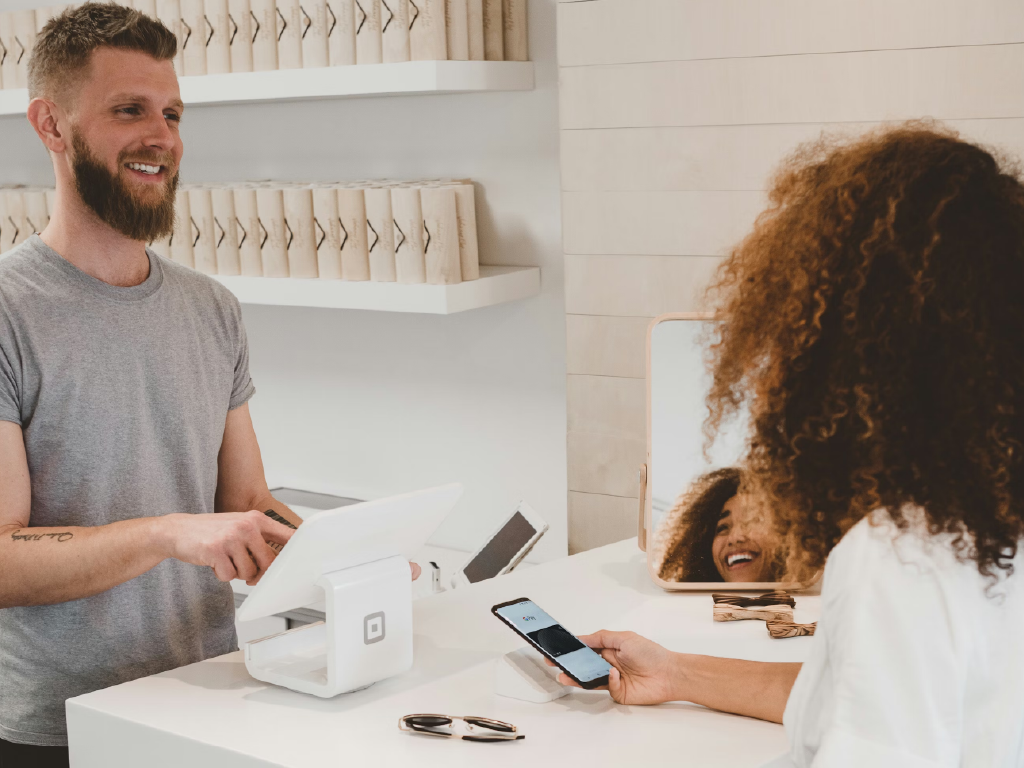 Homem sorridente realizando pagamento com Pix, atendente no caixa, ambiente moderno e bem iluminado, cliente usando celular.