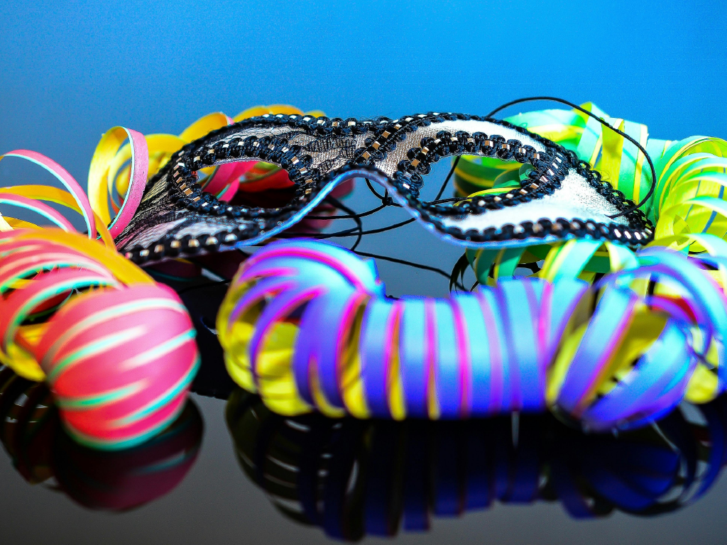 Imagem de carnaval com máscaras e serpentinas coloridas, refletindo cores vibrantes diante de um fundo azul. Perfeito para temas de festa, folia e celebrações.