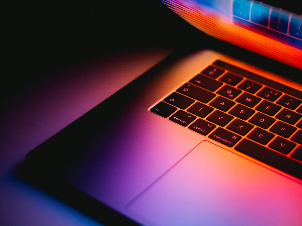 Imagem de um teclado de laptop iluminado com luzes laranja e roxas, destacando as teclas teclados com luz de fundo para tecnologia e inovação.